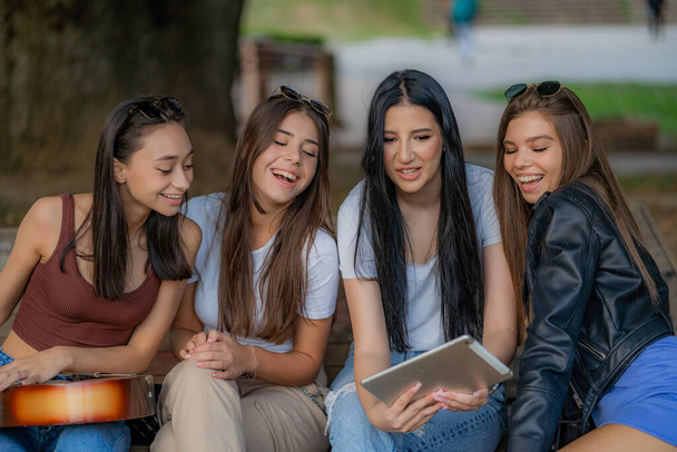 Cuatro chicas se ríen todas juntas mientras ven los divertidos videos en la tableta - Foto, Imagen