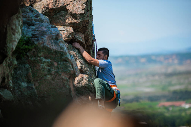 Mann greift nach Griff, während er an einer steilen Klippe klettert - Foto, Bild