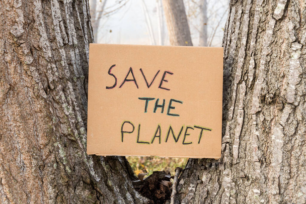Male hands hold a cardboard sign with the slogan -Save the Planet-, with natural wooded background. - Photo, Image