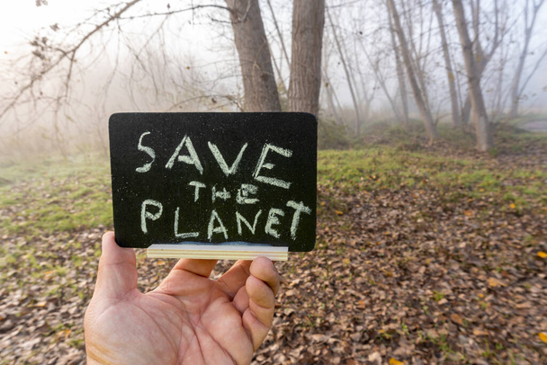 Male hand with small blackboard with the slogan written -Save the Planet-, with a background of brown leaves on the ground. - Φωτογραφία, εικόνα