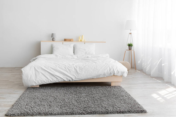 Podwójne łóżko, miękki szary dywan i lampa na podłodze, meble z akcesoriami, okno z zasłonami - Zdjęcie, obraz