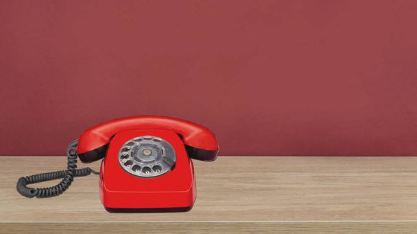 винтажный красный телефон, стоящий на деревянном полу перед красной стеной - Фото, изображение