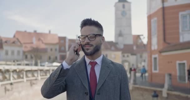 hombre de negocios guapo hablando por teléfono, usando anteojos y sonriendo a la cámara - Imágenes, Vídeo