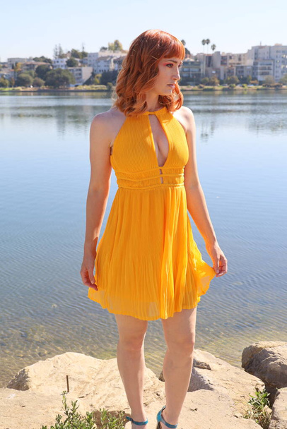 Photo of a Beautiful white girl in a beautiful dress standing in front of a lake - Fotó, kép