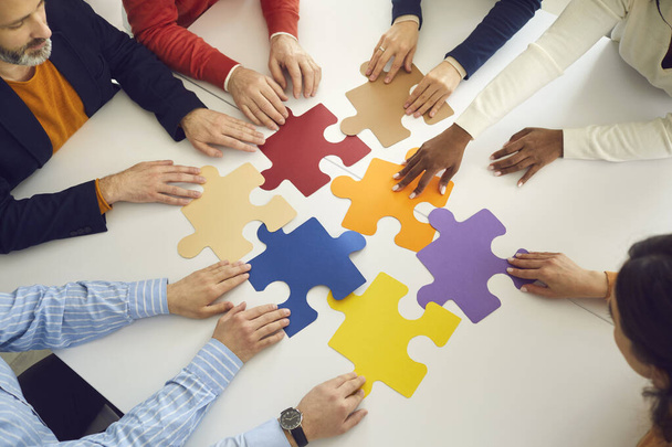 Multinationale Teamkollegen gruppieren von Hand bewegte Puzzleteile auf Bürotisch - Foto, Bild
