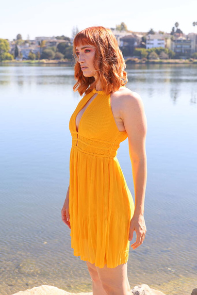 Photo of a Beautiful white girl in a beautiful dress standing in front of a lake - Foto, afbeelding