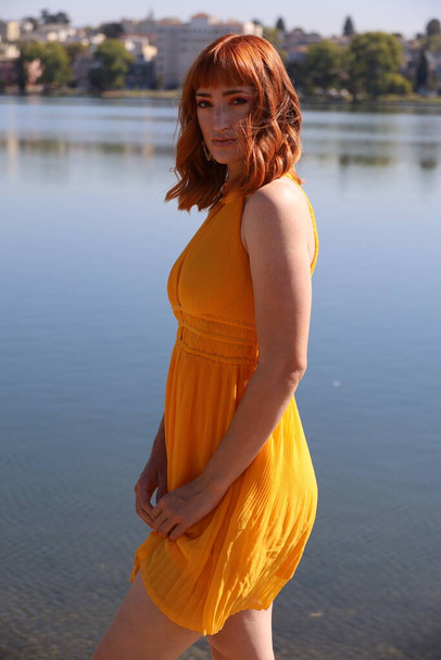 Photo of a Beautiful white girl in a beautiful dress standing in front of a lake - Fotó, kép