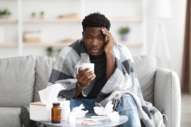 Upset black man having flu, drinking warm tea - Fotó, kép