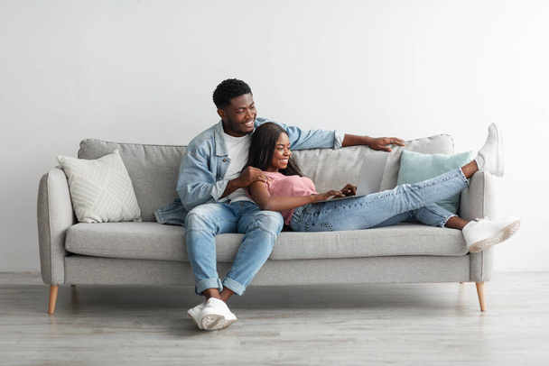 African American couple sitting on comfy couch, using pc - Foto, Imagen