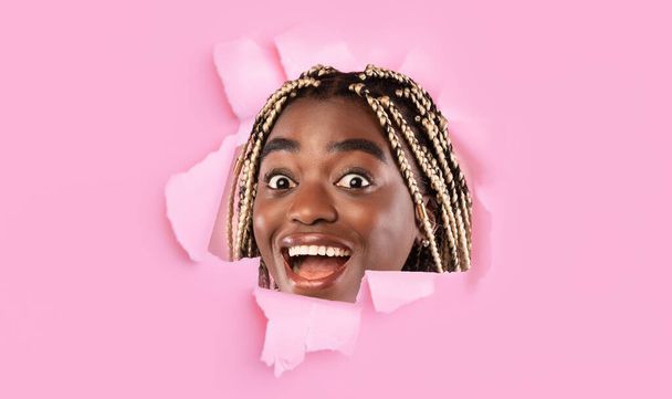 Śmieszny uśmiech millenium Afroamerykanka patrzy przez dziurę w różowym papierze, collage, panorama - Zdjęcie, obraz