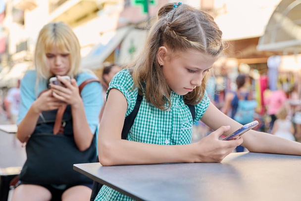 Preteen schoolgirl and teenage student with backpacks using smartphones, outdoor - Fotoğraf, Görsel