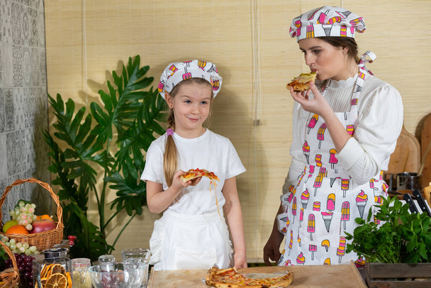 A mother with her five-year-old daughter are eating a pizza prepared and baked by them. Family home-made pizza tasting. After working together in the kitchen, its time to eat together. - Foto, Bild