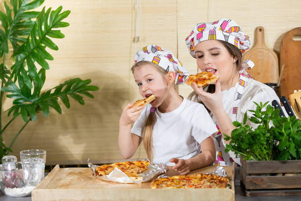 The five-year-old daughter sat down on her mothers lap and together they eat pizza made and baked by themselves. After working together in the kitchen, its time to eat together. - Photo, image