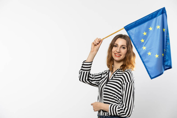 Young attractive girl with the flag of the European Union. A student holds the European Union flag in her hand. Woman with flag on white background. Isolated from the background. - Photo, Image