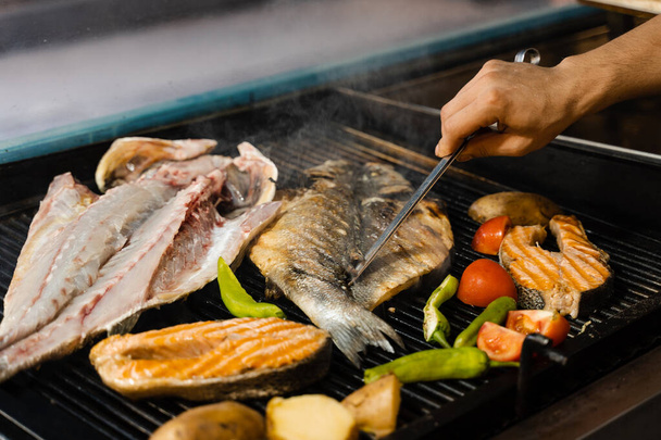 Cocinar mariscos mezcla de salmón, lubina y verduras. Pescado a la parrilla con patatas con chile y tomate - Foto, Imagen