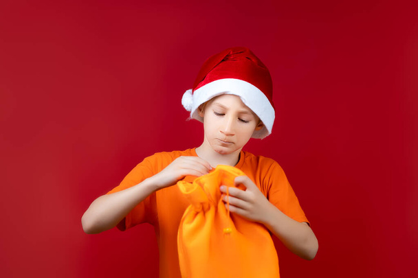 nas mãos de um menino que está usando um chapéu de Papai Noel, um saco de presente amarelo que ele quer abrir - Foto, Imagem