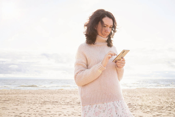 Ihmiset elävät sosiaalisessa mediassa. Tyttö kävelee meren rannalla matkapuhelimen kanssa. Riippuvuus vempaimista nuorten keskuudessa. - Valokuva, kuva