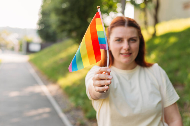Gyönyörű piros leszbikus nő LMBT szivárvány zászló naplementekor zöld természet háttér. Boldogság, szabadság és szerelem koncepció azonos nemű párok számára. - Fotó, kép