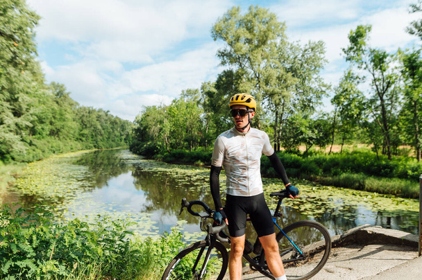 Portrait of a cyclist athlete on vacation while riding in the woods, standing on the background of the river and looking away with a serious face. - Photo, Image