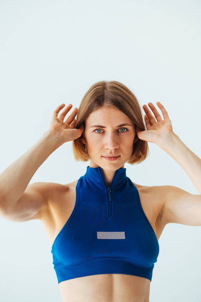 Портрет спортивной женщины в синем топе на белом фоне, позирующей перед камерой с серьезным лицом. Вертикаль. - Фото, изображение