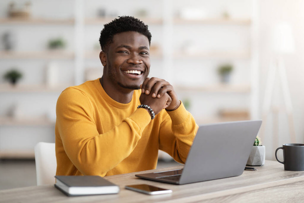 Black man freelancer sitting at workdesk at home, using laptop - Foto, Bild