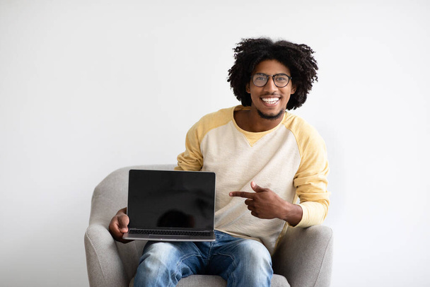 椅子に座っている間にブランクノートパソコンの画面を指して陽気な黒人男 - 写真・画像