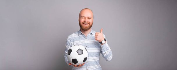 Веселый мужчина в непринужденной позе держит шарик и показывает большой палец вверх - Фото, изображение