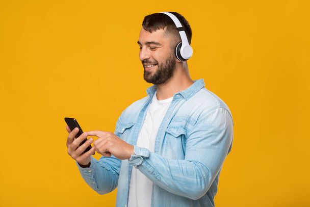 Feliz adulto europeo chico en auriculares disfrutando de la música favorita, escribiendo en el teléfono inteligente - Foto, imagen