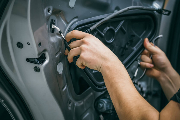 Работник автосервиса демонтирует дверь автомобиля для ремонта, восстановления, настройки звука автомобиля или установки шумоизоляции или звукоизоляции - Фото, изображение