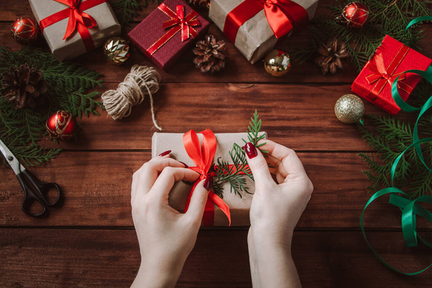 Proceso de envoltura de regalo de Navidad. Mujer decora caja con una cinta roja. - Foto, Imagen