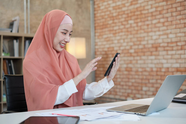 Beautiful businesswoman who Islamic female person is talking on her mobile phone communication and happy smiling because internet online order in laptop, modern lifestyle, e-commerce occupation. - Photo, Image