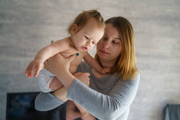 Bebé y madre mujer caucásica adulta sostienen a su hija de seis meses de edad niña en la habitación con pijamas en la mañana en el hogar paternidad familia vida doméstica concepto de vinculación personas reales copiar espacio - Foto, imagen