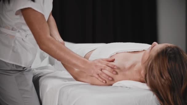 Mujer joven teniendo una sesión de masaje tumbada en el sofá mientras la masajista trabaja con su brazo - Imágenes, Vídeo