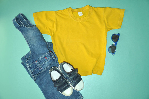 T-shirt jaune pour enfants avec jean bleu et baskets sur fond bleu - Photo, image