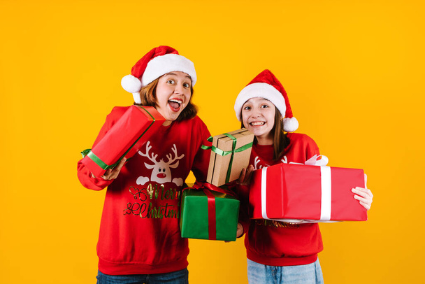Portrait of Latin sisters girls holding Christmas gift box on a yellow background in Mexico latin america - Photo, Image