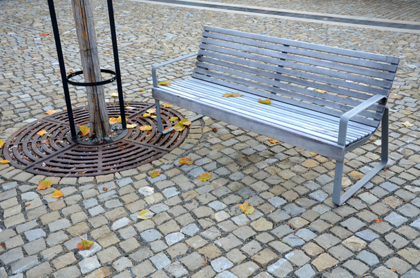 скамейки на мощеной площади с песчаной поверхностью из уплотненного гравия. обледенение стальная темно-серая мебель для посетителей. стальные решетки в форме круга позволяют деревьям расти на тротуаре - Фото, изображение