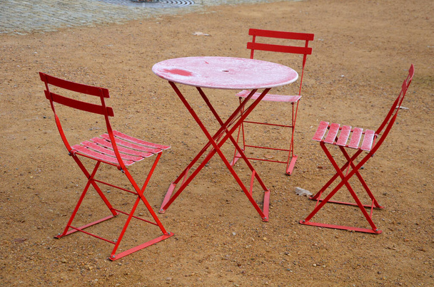 punaiset tuolit ja pyöreät pöydät kahvilassa mukulakivikerroksella, jonka hiekkapinta on tiivistettyä soraa. kaikki on valmistettu kevyestä materiaalista, joka voidaan taittaa ja puhdistaa joka ilta. jääkuorrutus - Valokuva, kuva
