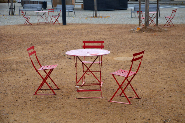 Piros székek és kerek asztalok egy kávézóban egy macskaköves téren, homokfelülettel, tömörített kavicsból. minden olyan fényanyagból készül, amit minden este össze lehet hajtogatni és tisztítani. jegesedés - Fotó, kép