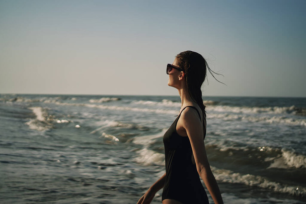 woman in black swimsuit walking on the beach ocean summer - Фото, зображення
