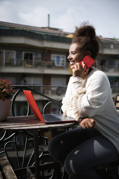 Femme parlant sur le téléphone portable tout en travaillant sur un balcon à la maison. - Photo, image