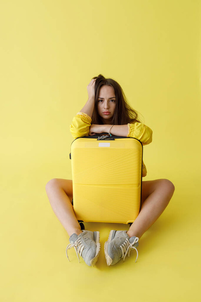 Χαριτωμένη νεαρή γυναίκα με ταξιδιωτική τσάντα κάθεται στο στούντιο - Φωτογραφία, εικόνα