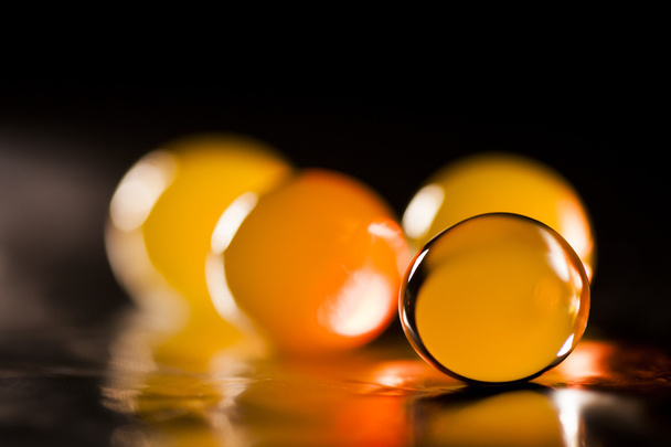 Abstract composition with beautiful, orange, round jelly balls on an aluminium foil with reflexions and dark background - 写真・画像