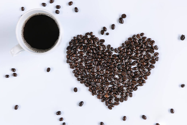 Filiżanka kawy i palona kawa Fasola Kształt serca na białym odizolowanym tle, zbliżenie ziarna kawy składników z gorącej kawy tła filiżanki. Pojęcia żywności i napojów - Zdjęcie, obraz