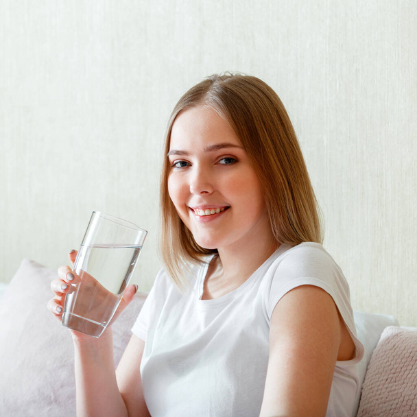 Smile young woman drinks glass of pure water in morning after waking up in her bed room. Happy teen girl maintains water balance for body health by drinking clean water. square close up Portrait - Foto, Imagem