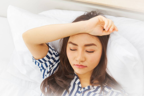Retrato durmiendo Asiática adolescente, pero todavía pensando mientras se relaja en la cama: Coast-up, la joven mujer puso las manos en la cabeza, todavía fingiendo dormir y todavía no quería levantarse de la cama. - Foto, imagen
