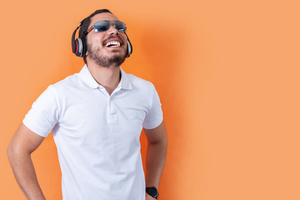 A cheerful young man with beard and sunglasses, listening to music with wireless headphones - Fotoğraf, Görsel