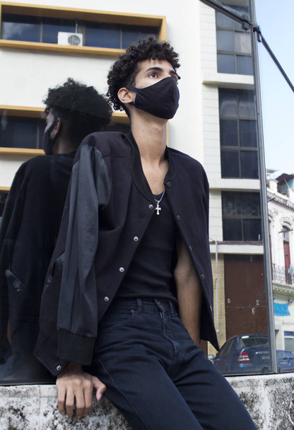 A young Hispanic male in a black outfit and face mask posing on the streets in Old Havana, Cuba - Foto, afbeelding