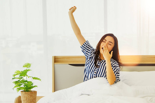 Retrato meninas asiáticas vestindo pijama, usando as mãos para fechar a boca, bocejando, apenas acordar e esticar os braços para relaxar de manhã no quarto. - Foto, Imagem