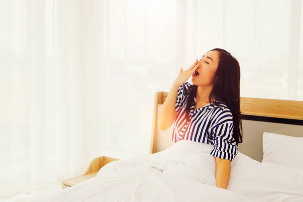 Asian woman stayed up late, a chain reaction woke up, was drowsy, sat yawning, covered her mouth with her hands and wanted to continue sleeping : Not getting enough sleep concept - Foto, Imagem