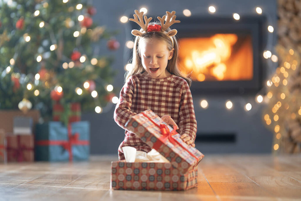 Merry Christmas and Happy Holidays! Cheerful cute child girl with gift. Kid is having fun near tree.     - Foto, Bild